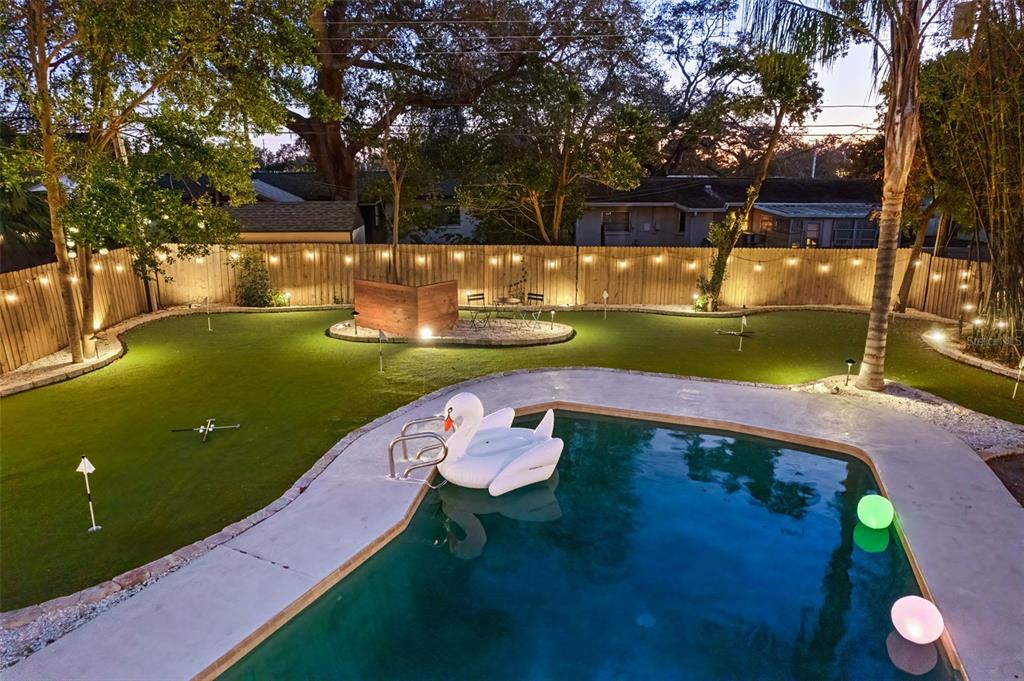 An outdoor backyard features a swimming pool, a putting green, and string lights at dusk — 13672 88TH AVENUE, SEMINOLE, FL