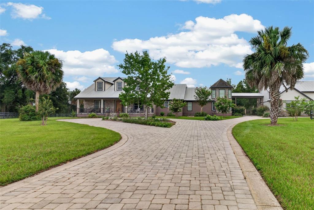 A paved driveway leads to a large house with a metal roof and stone facade — 13342 W LAKE YALE ROAD, UMATILLA, FL