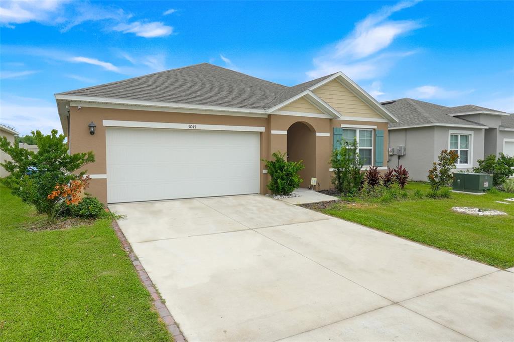 A single-story house with a tan stucco exterior, a two-car garage, and a concrete driveway — 3041 TOBAGO DRIVE, HAINES CITY, FL