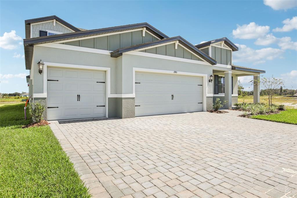 A light green house with a three-car garage and a paved driveway under a blue sky — 1740 DRAUGHTON DRIVE, ZEPHYRHILLS, FL