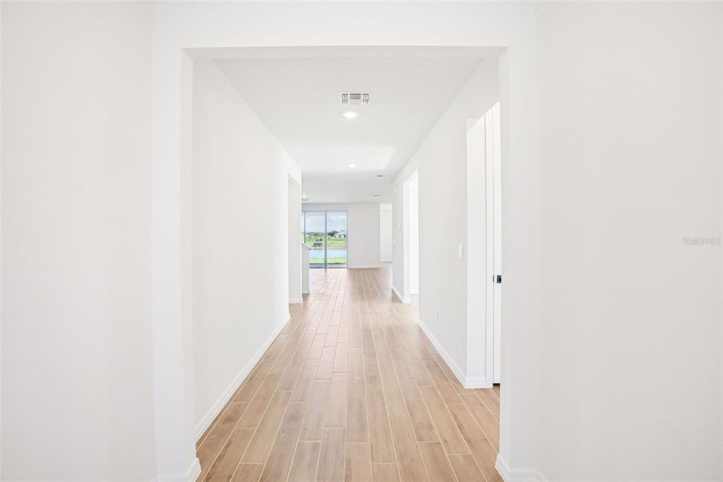 A bright hallway with light wood-look tile flooring leads toward a glass sliding door — 1740 DRAUGHTON DRIVE, ZEPHYRHILLS, FL
