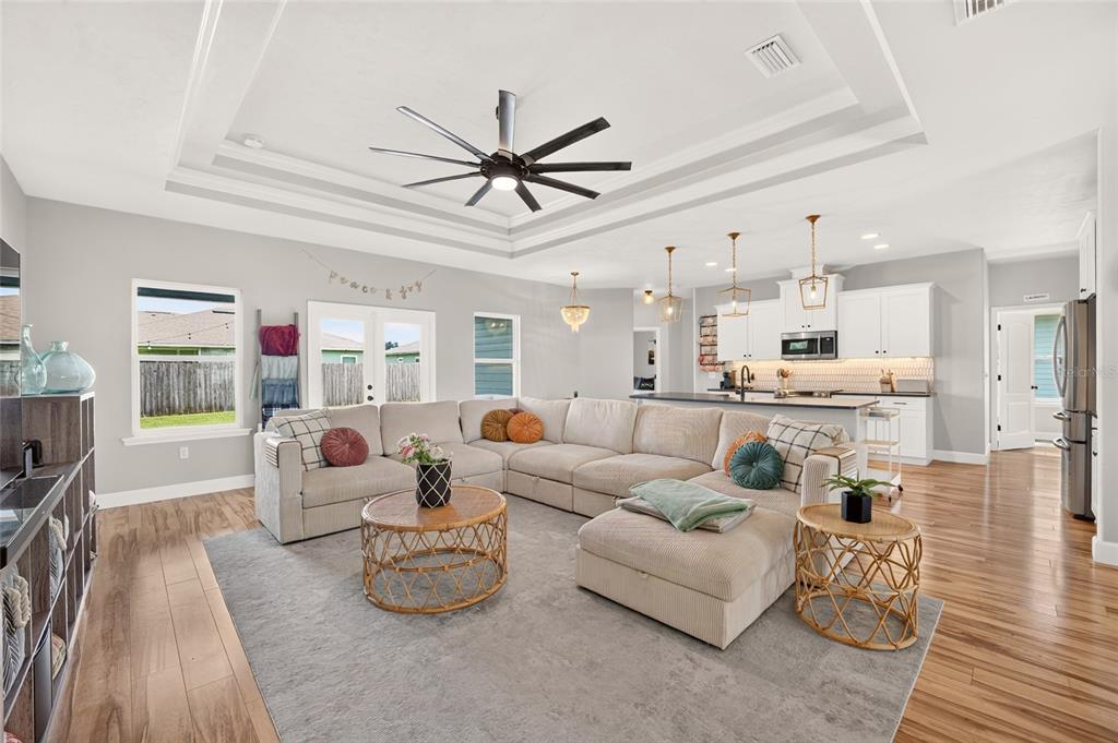 A spacious open-concept living room features a large sectional sofa, tray ceiling, and kitchen area — 23038 NW 4TH PLACE, NEWBERRY, FL