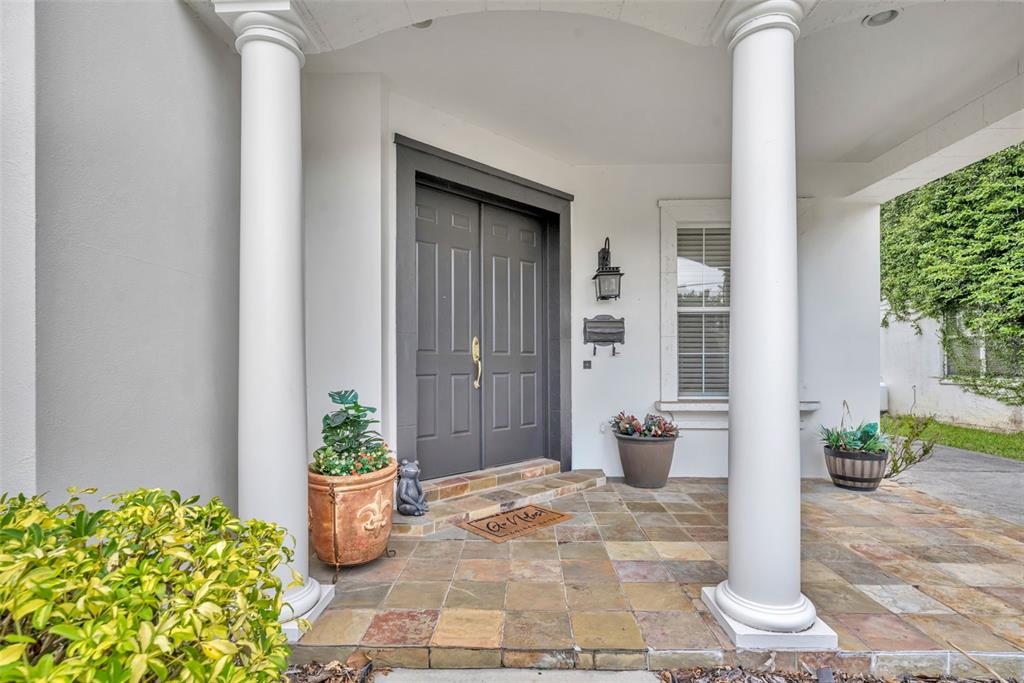 A covered front porch features stone tile flooring, white columns, and a dark double door — 1031 GUERNSEY STREET, ORLANDO, FL