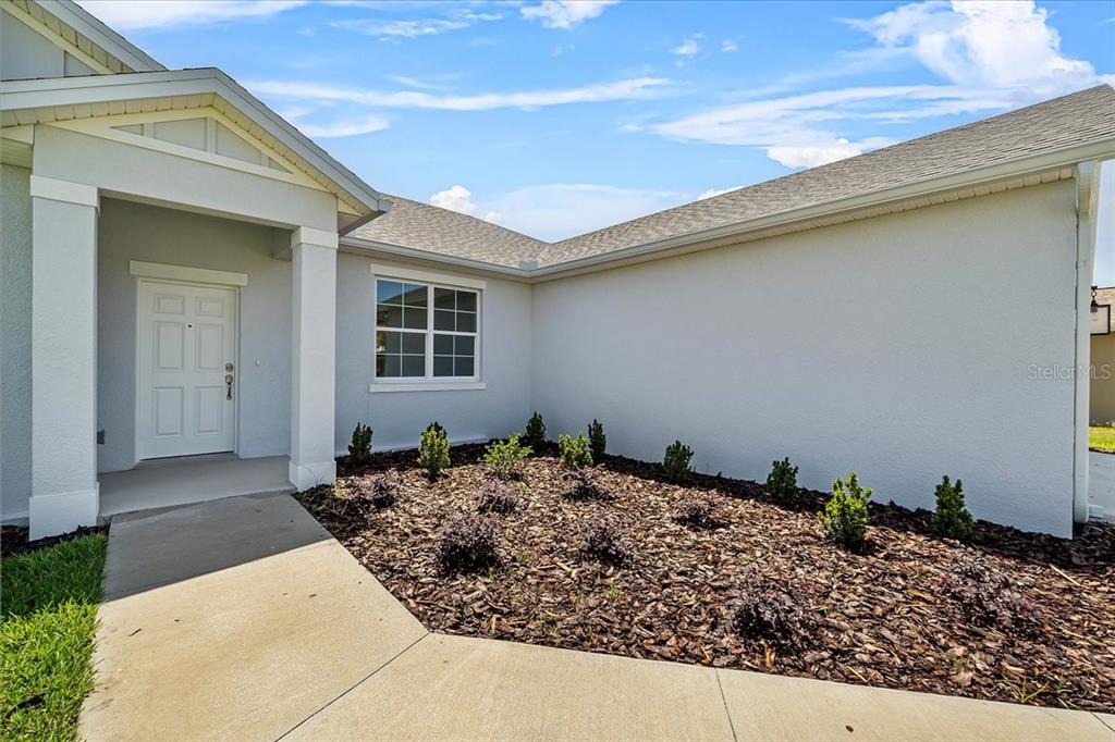 A concrete walkway leads to the front entrance of a house with light-colored stucco walls — 4502 FAIRWAY OAKS DRIVE, MULBERRY, FL