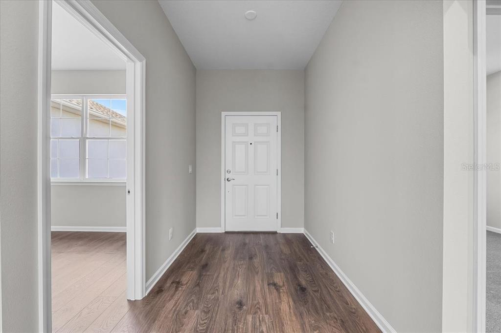 A hallway with wood-look flooring leads to a white door with a window — 4502 FAIRWAY OAKS DRIVE, MULBERRY, FL