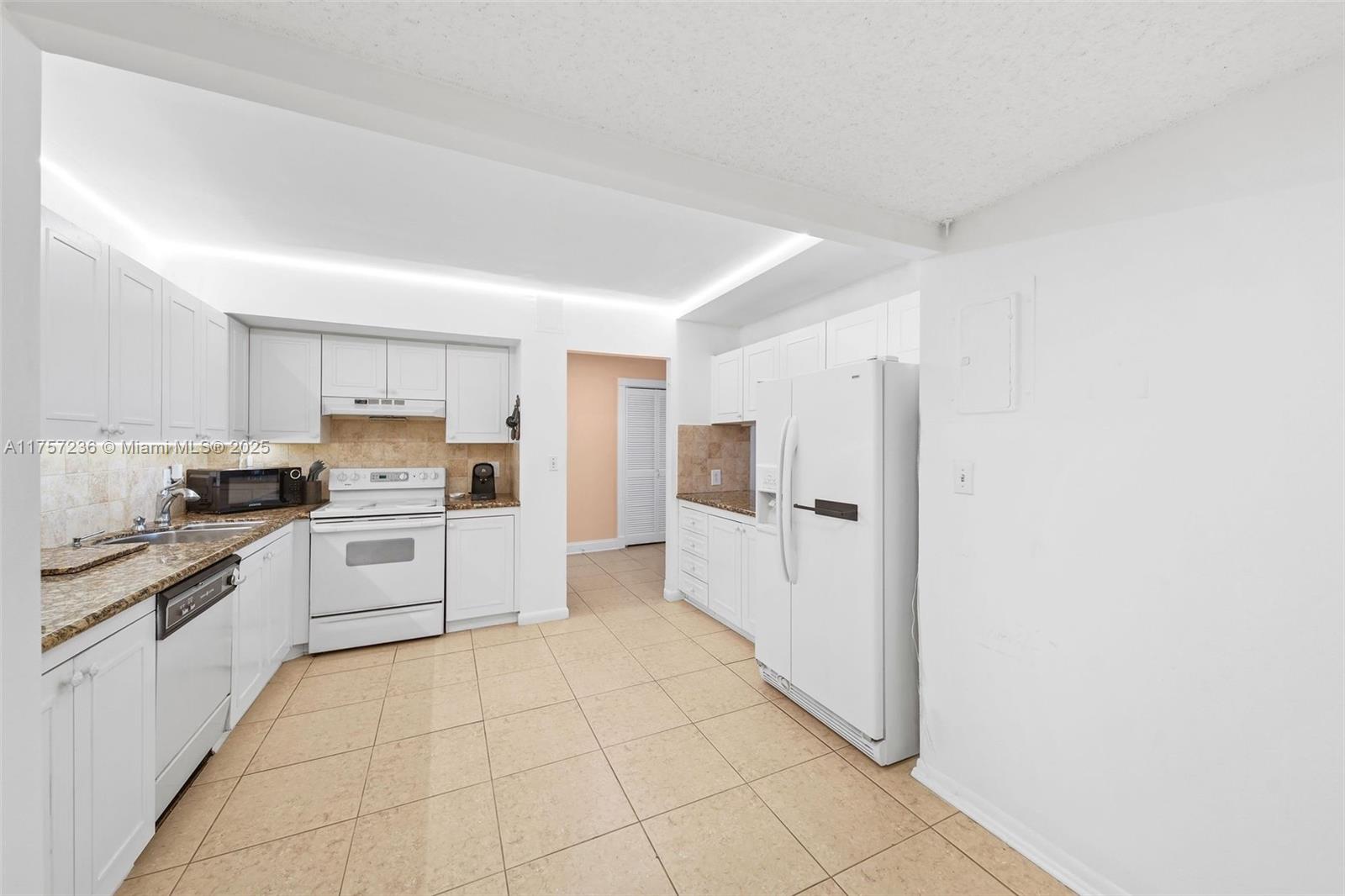 A kitchen features white cabinetry, tan tile flooring, granite countertops, and white appliances — 2500 Parkview Dr # 812, Hallandale Beach FL 33009, HALLANDALE BEACH, FL