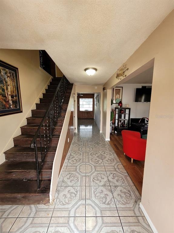 A tiled entryway features a wooden staircase with a black metal railing and a living area — 5891 SIR HENRY ROAD, ORLANDO, FL