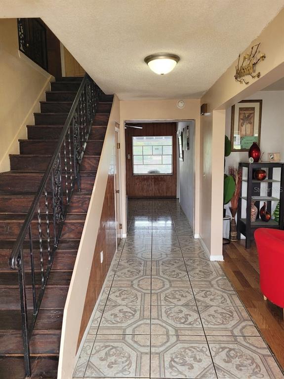A hallway with tiled flooring leads to a room with wood paneling and a staircase — 5891 SIR HENRY ROAD, ORLANDO, FL