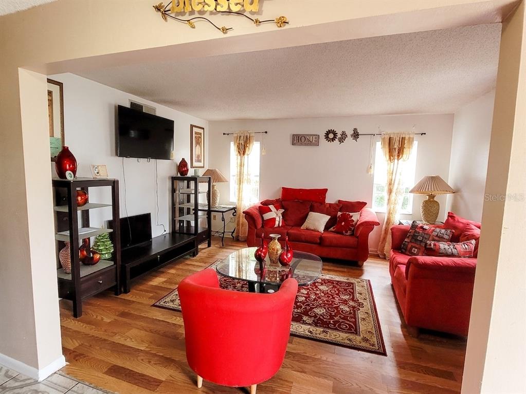 A living room features red sofas, a glass coffee table, and wood-look flooring — 5891 SIR HENRY ROAD, ORLANDO, FL