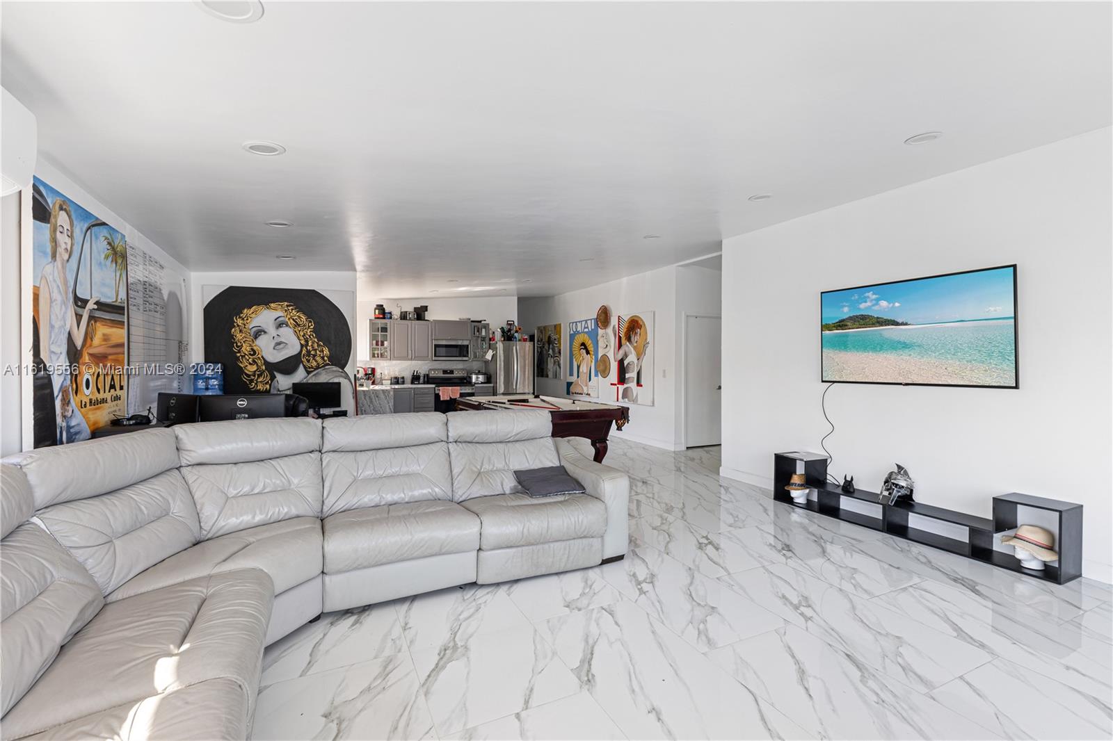 A living room features a white leather sectional, marble-look tile floors, and a wall-mounted television — 8221 Crespi Blvd, Miami Beach FL 33141, MIAMI BEACH, FL