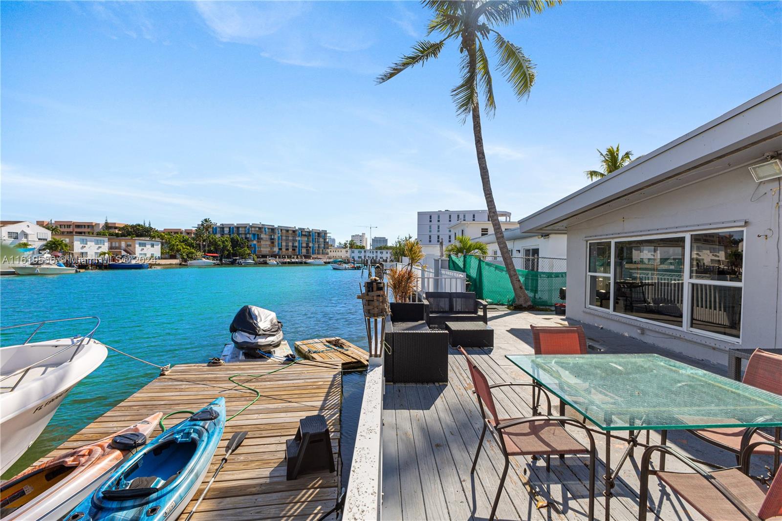 A wooden deck with outdoor furniture and a dock sits beside a canal — 8221 Crespi Blvd, Miami Beach FL 33141, MIAMI BEACH, FL