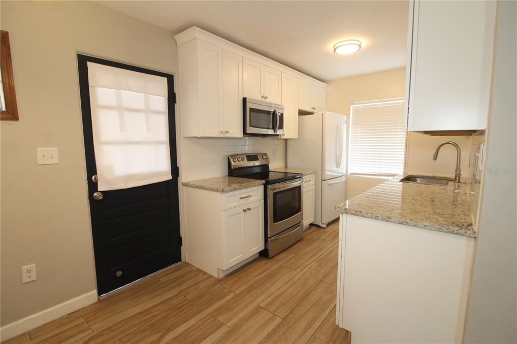 A kitchen features white cabinets, granite countertops, stainless steel appliances, and wood-look tile flooring — 207 LAKE VIEW DRIVE, SANFORD, FL