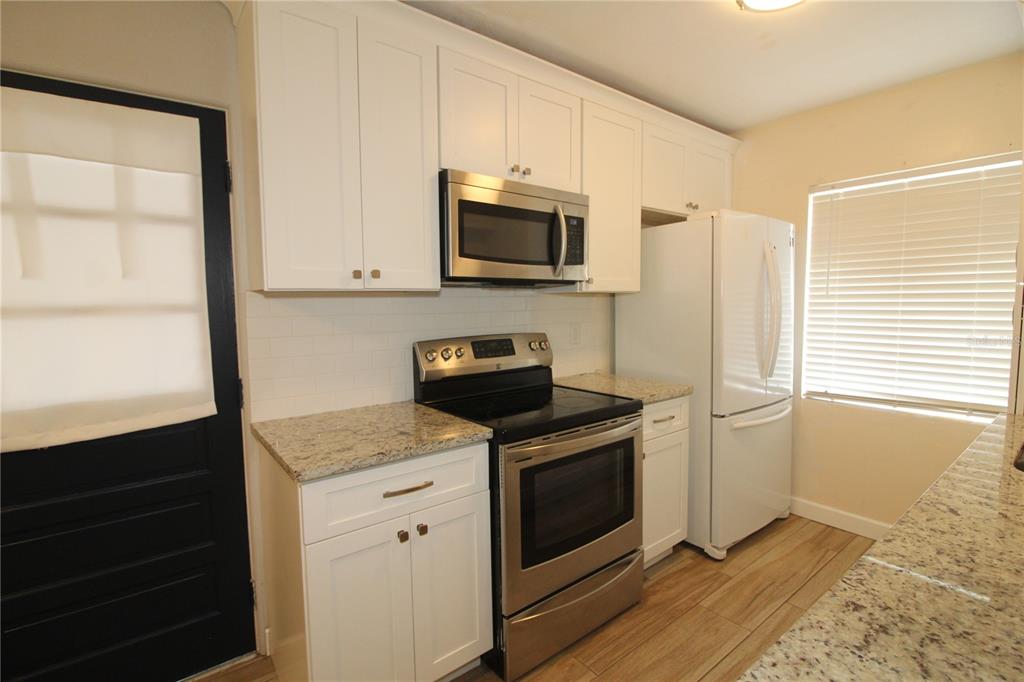 A kitchen features white cabinets, stainless steel appliances, granite countertops, and light wood-look flooring — 207 LAKE VIEW DRIVE, SANFORD, FL
