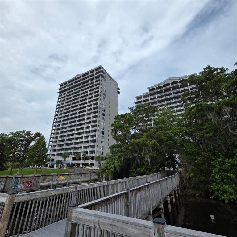 A wooden boardwalk leads toward two tall residential buildings surrounded by trees under a cloudy sky — 13415 BLUE HERON BEACH DRIVE UNIT 609, ORLANDO, FL