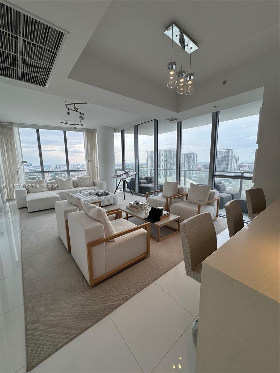 A modern living room features floor-to-ceiling windows, white tile flooring, and neutral-toned furniture — 1100 Biscayne Blvd # 2605, Miami FL 33132, MIAMI, FL
