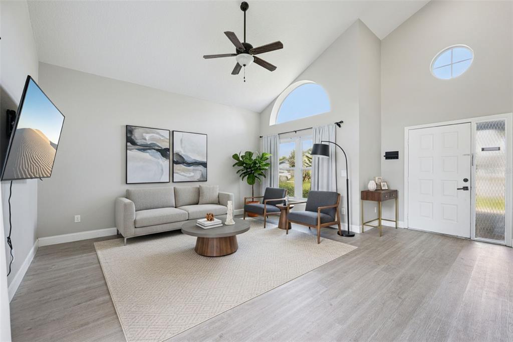A living room with light gray walls, wood-look flooring, a vaulted ceiling, and large windows — 622 COLORADO WOODS COURT, ORLANDO, FL