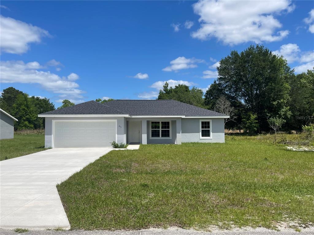 A single-story house with a tan stucco exterior, a two-car garage, and a concrete driveway — 200 FISHER ROAD, OCKLAWAHA, FL