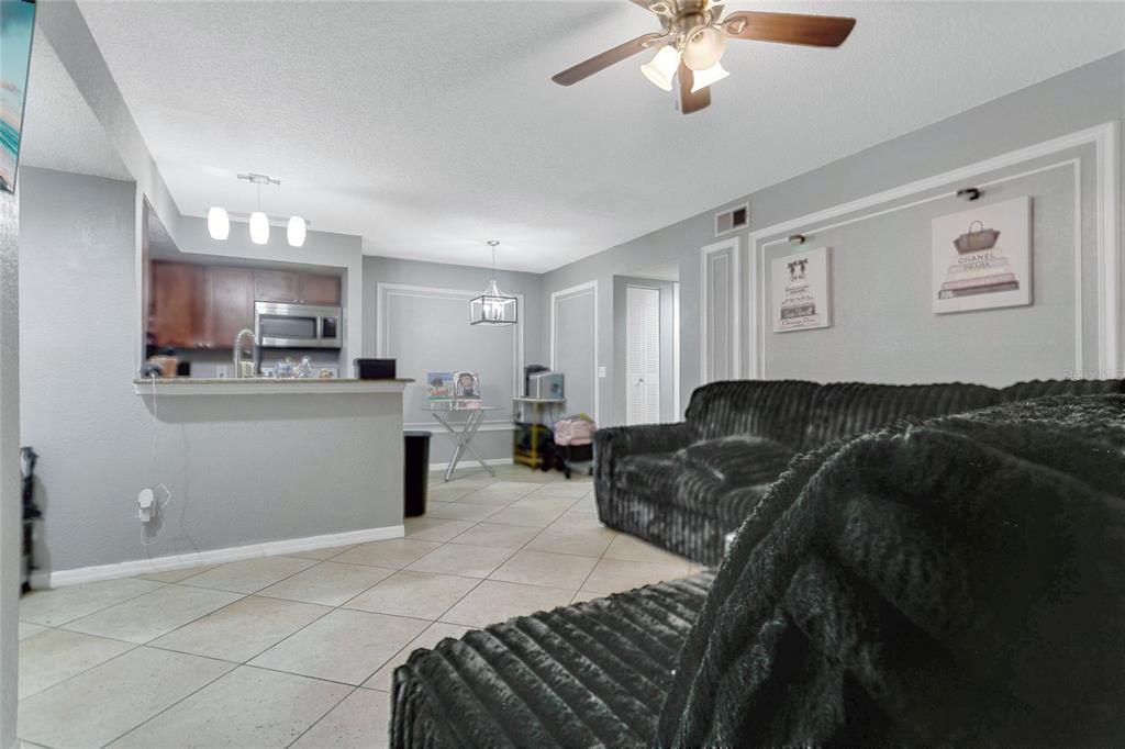A living room with tile flooring, a black sofa, and an open kitchen with bar seating — 5148 CONROY ROAD UNIT 12, ORLANDO, FL