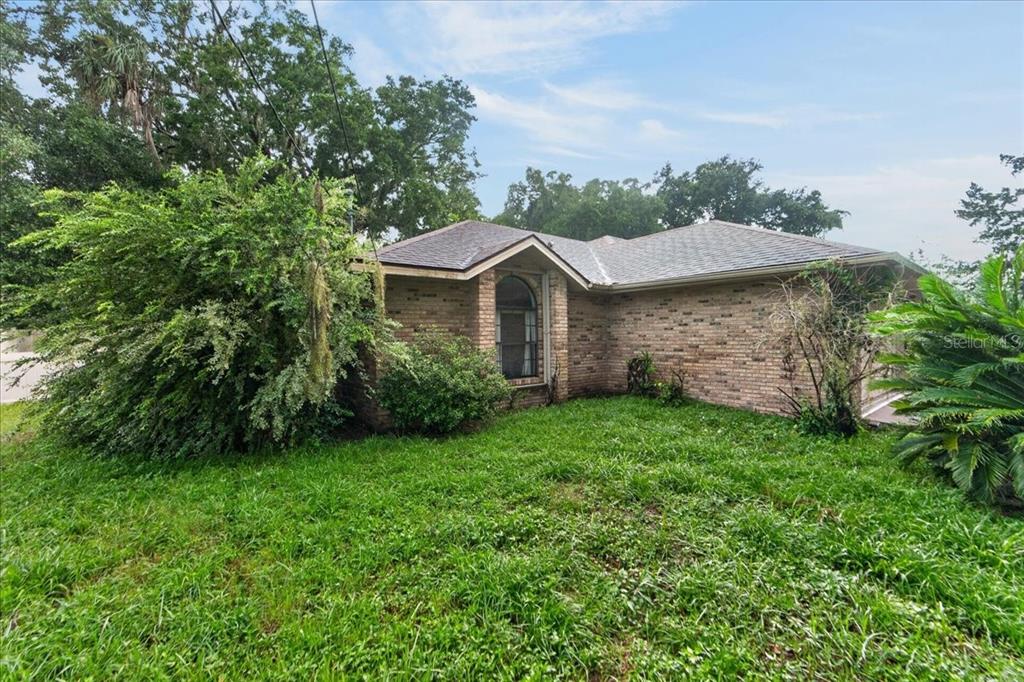 A single-story brick house with a prominent arched window and overgrown landscaping — 344 N FREDERICK AVENUE, DAYTONA BEACH, FL