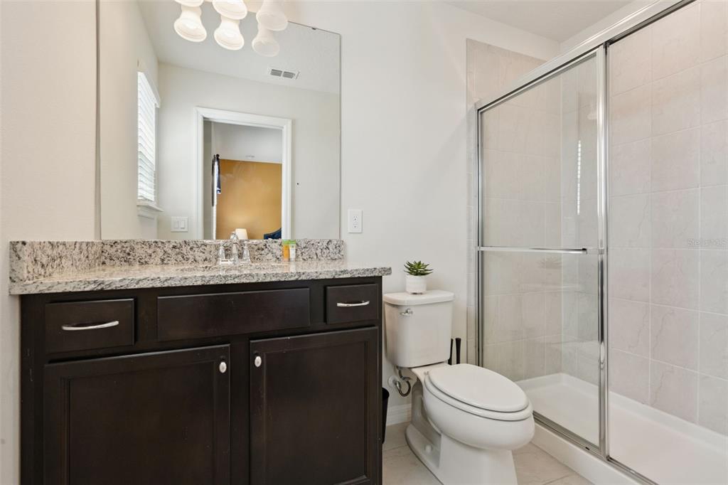 A bathroom features a dark wood vanity with a granite countertop, toilet, and glass shower — 1876 SUMMER DRIVE, DAVENPORT, FL