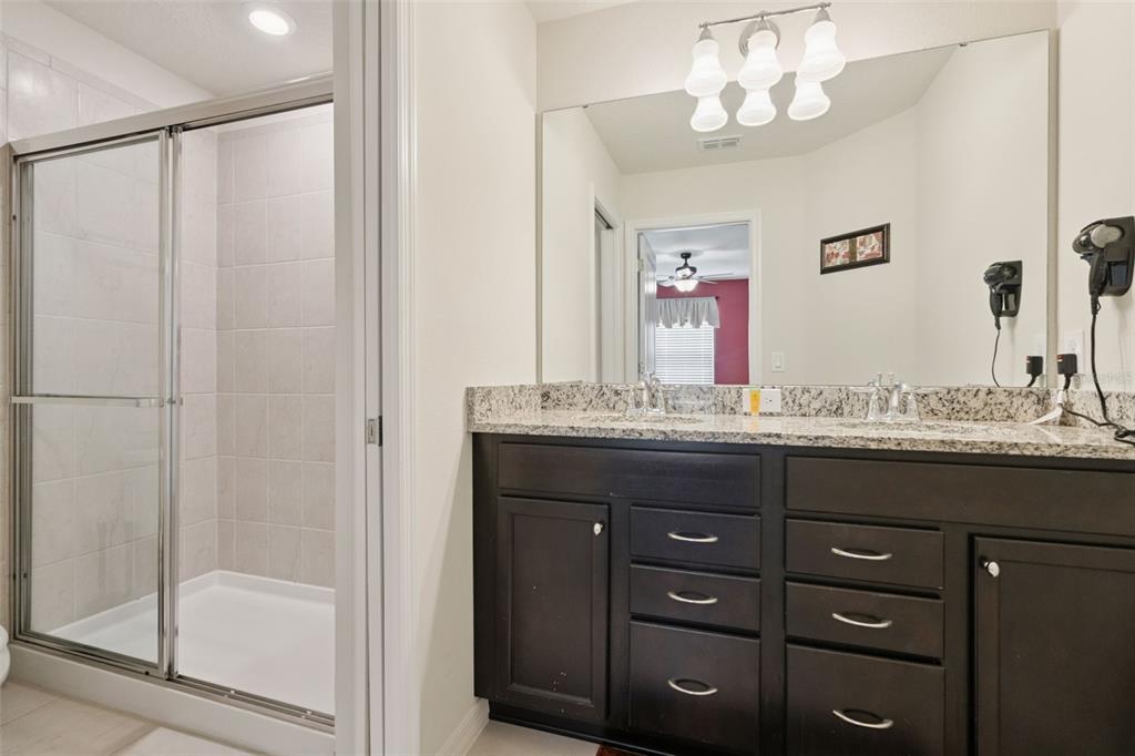 A bathroom features a dark wood double vanity with granite countertops and a glass shower — 1876 SUMMER DRIVE, DAVENPORT, FL