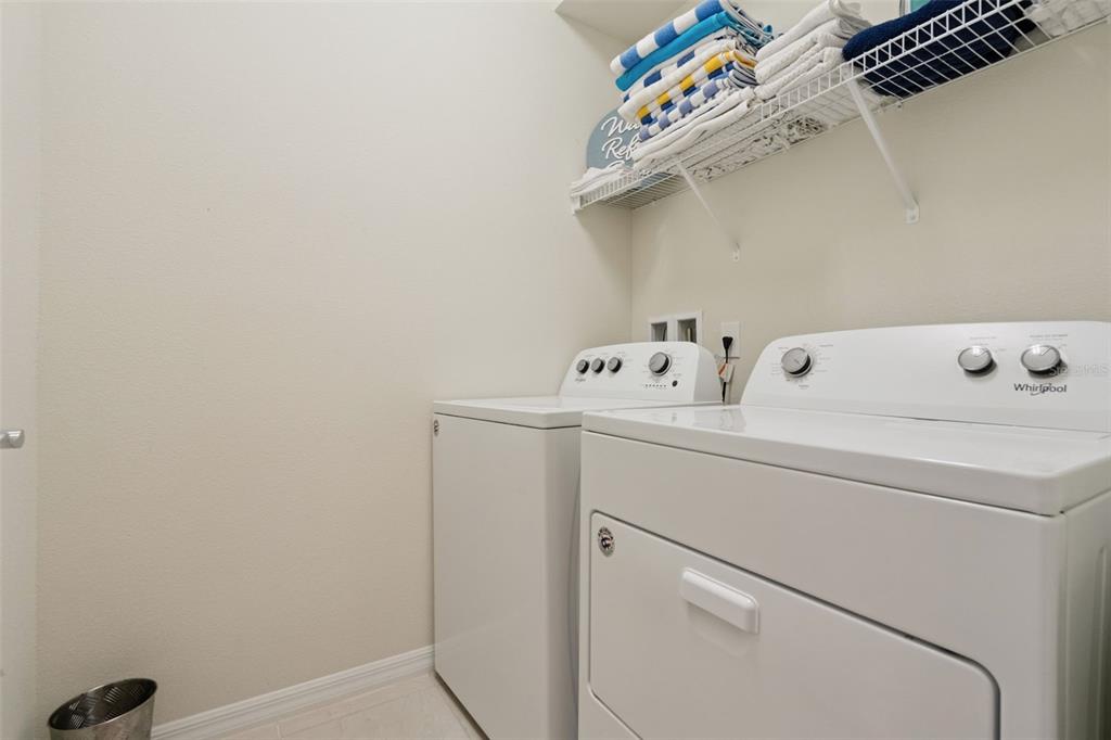 A laundry room features white appliances, a wire shelf with towels, and a trash can — 1876 SUMMER DRIVE, DAVENPORT, FL