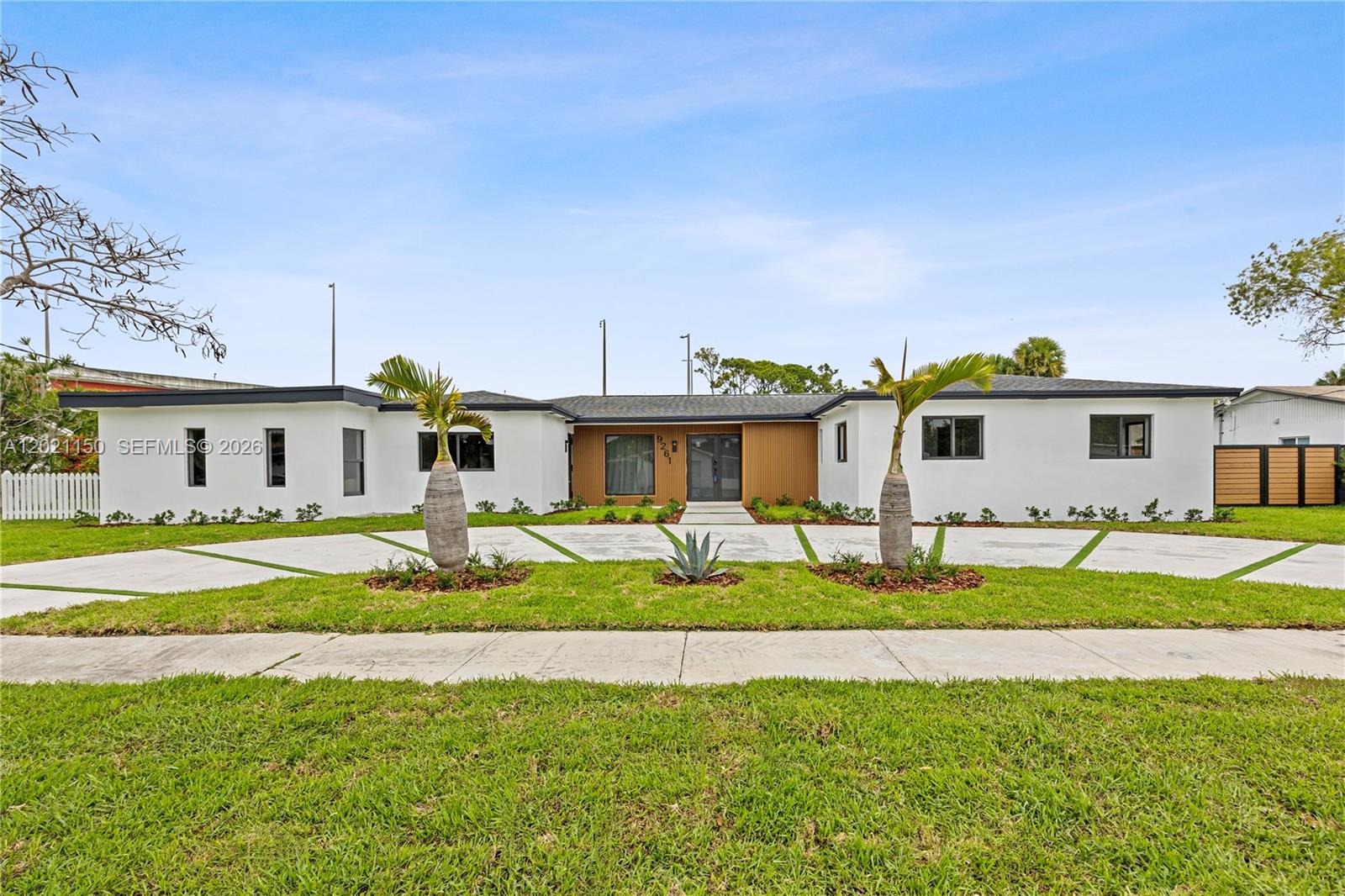 A single-story white house features a modern wood-paneled entryway and a wide concrete driveway — 9261 SW 80th Ter, Miami FL 33173, MIAMI, FL