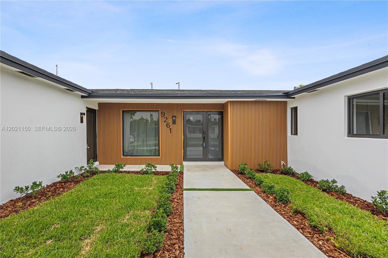 The exterior of a modern home features white walls, wood slat siding, and a walkway — 9261 SW 80th Ter, Miami FL 33173, MIAMI, FL