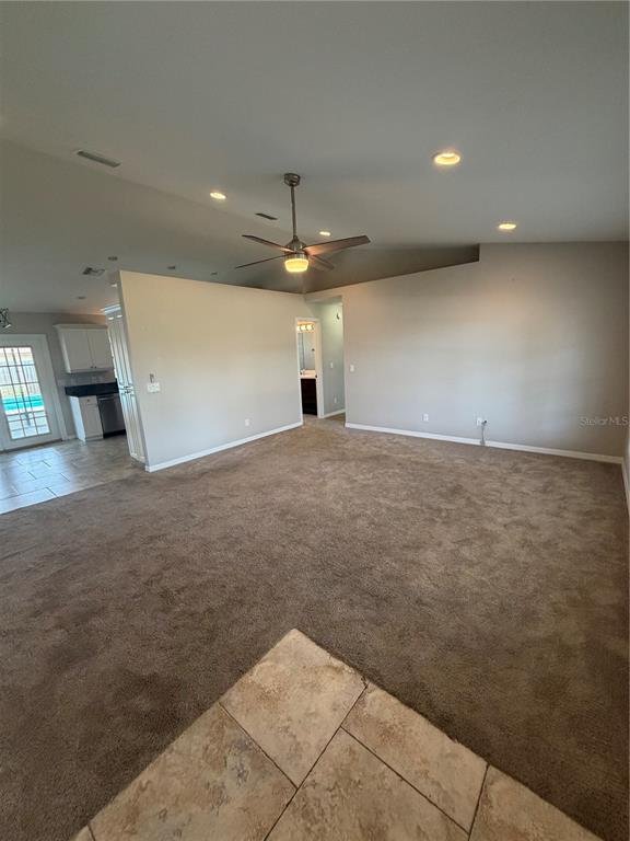 A carpeted living room features a ceiling fan, recessed lighting, and an adjacent tiled kitchen — 5741 SE 21ST LANE, OCALA, FL