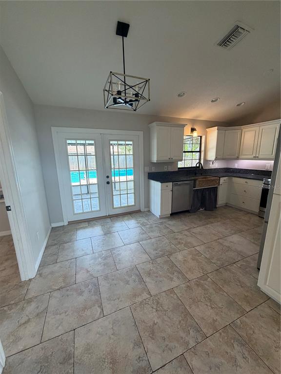 A kitchen with white cabinets, dark countertops, tile flooring, and French doors leading to a pool — 5741 SE 21ST LANE, OCALA, FL