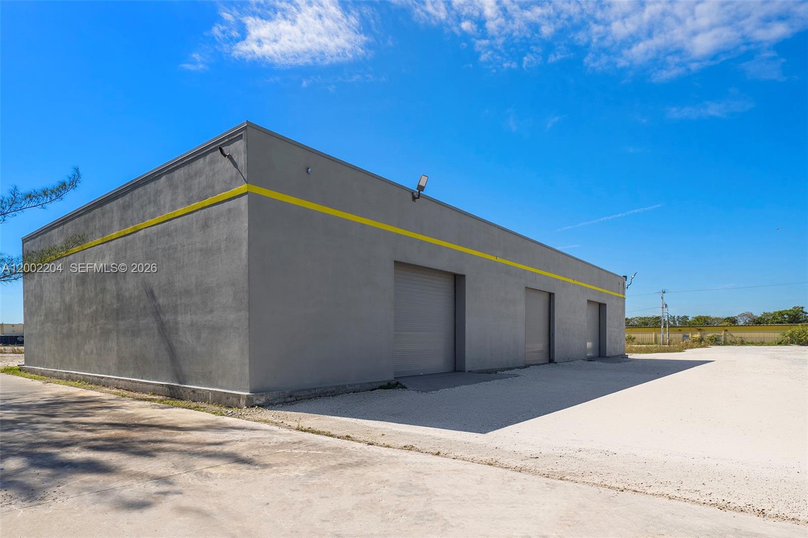 A gray industrial building with three roll-up doors and a yellow horizontal stripe — 3080 Sheridan St Warehouse + Office, Hollywood FL 33020, HOLLYWOOD, FL