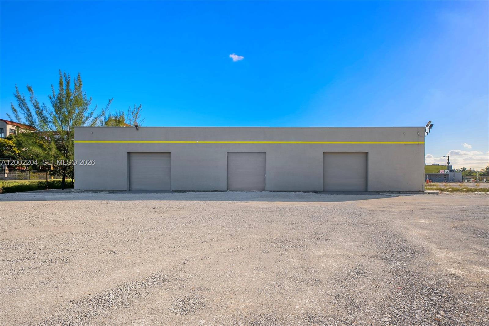 A gray industrial building features three roll-up doors and a yellow horizontal stripe — 3080 Sheridan St Warehouse + Office, Hollywood FL 33020, HOLLYWOOD, FL
