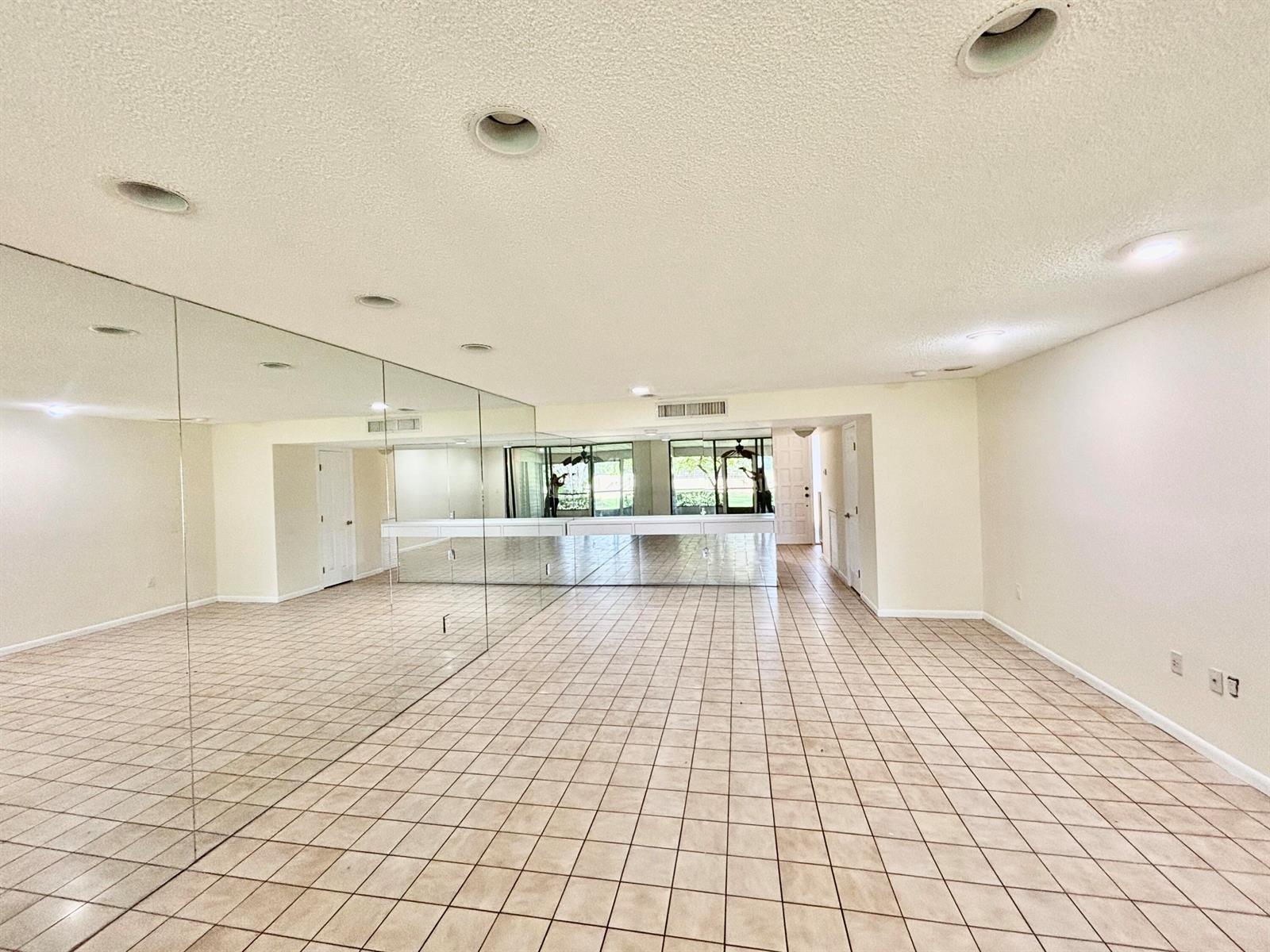 A spacious room features beige tile flooring, recessed lighting, and a wall of mirrored panels — 4807 Esedra Court, Lake Worth FL 33467, LAKE WORTH, FL
