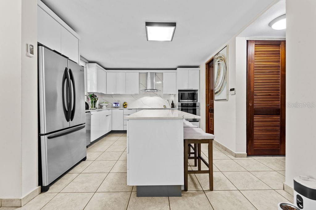 A modern kitchen features white cabinetry, stainless steel appliances, a central island, and tiled flooring — H2 MAR DE BERING UNIT 638, DORADO, PR
