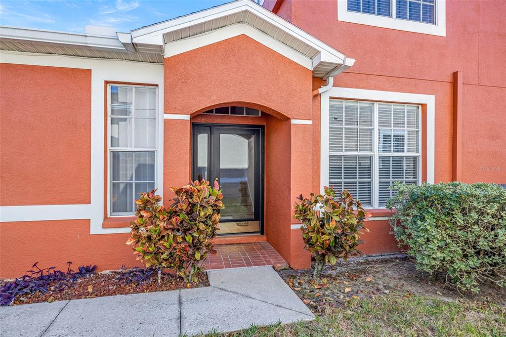 The exterior of a house features an orange stucco facade, a front door, and landscaping — 11016 BLAINE TOP PLACE, TAMPA, FL