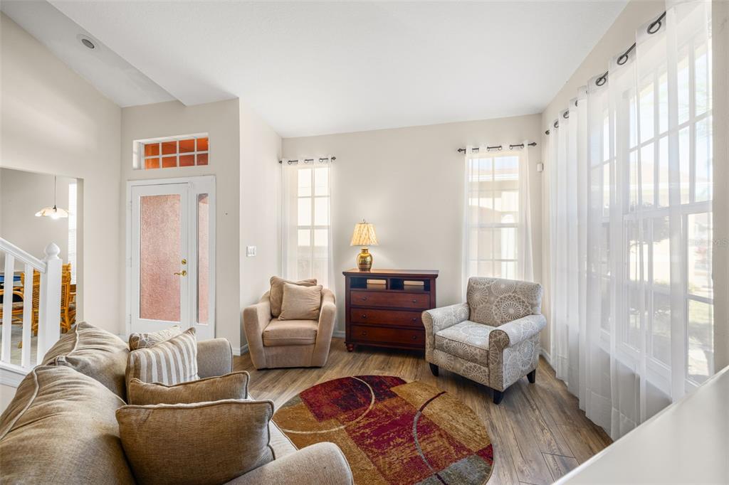 A living room features wood-look flooring, two armchairs, a wooden dresser, and large windows — 11016 BLAINE TOP PLACE, TAMPA, FL