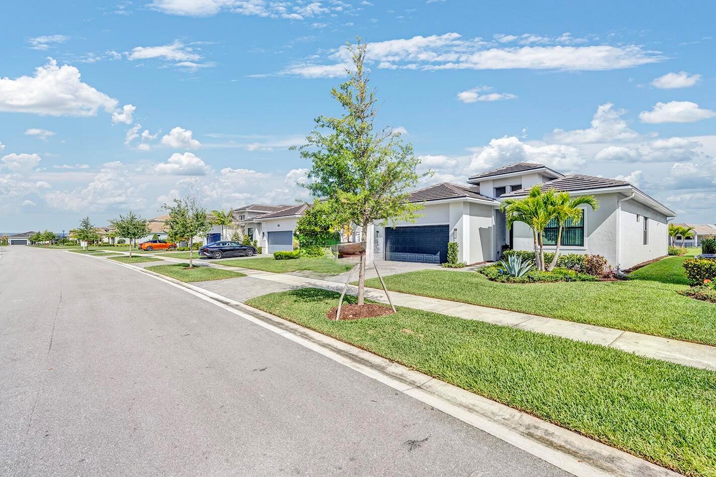 A suburban street view featuring a modern single-story house with a dark garage door — 15647 Merritt Drive, Westlake FL 33470, WESTLAKE, FL