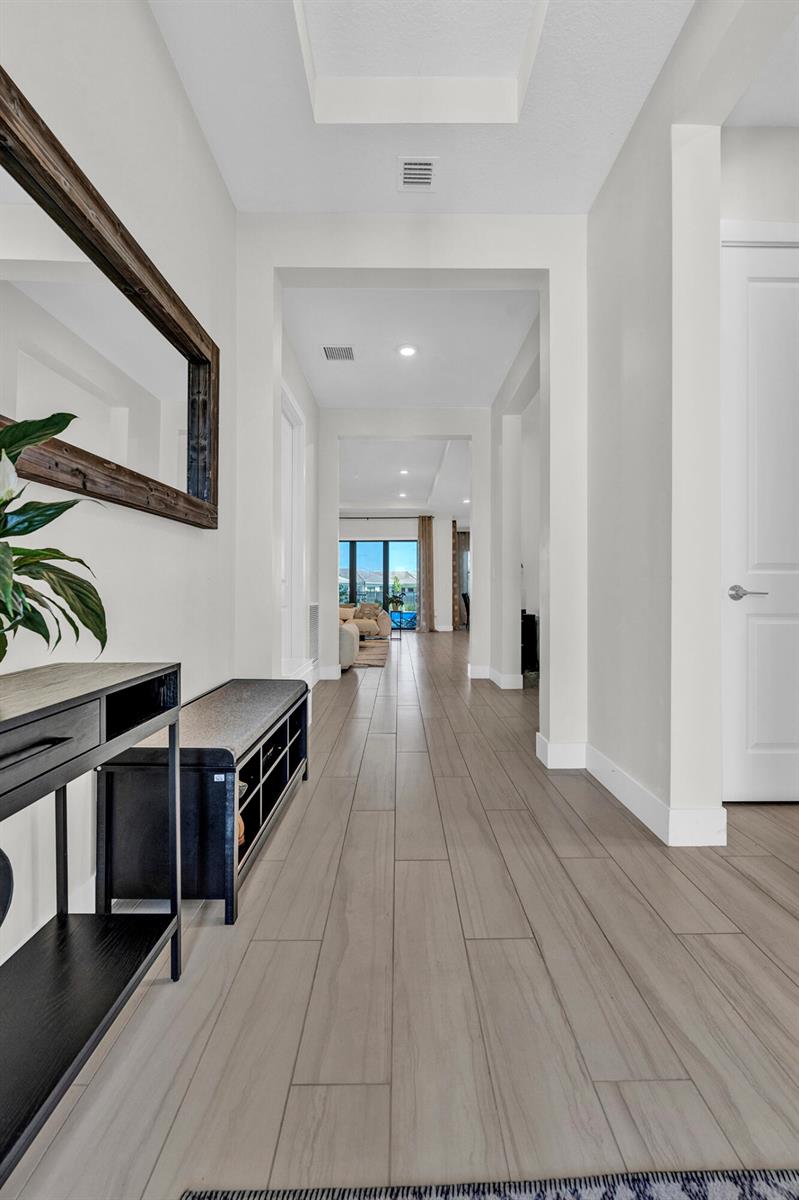 A bright hallway with light wood-look tile flooring leads toward an open living area — 15647 Merritt Drive, Westlake FL 33470, WESTLAKE, FL