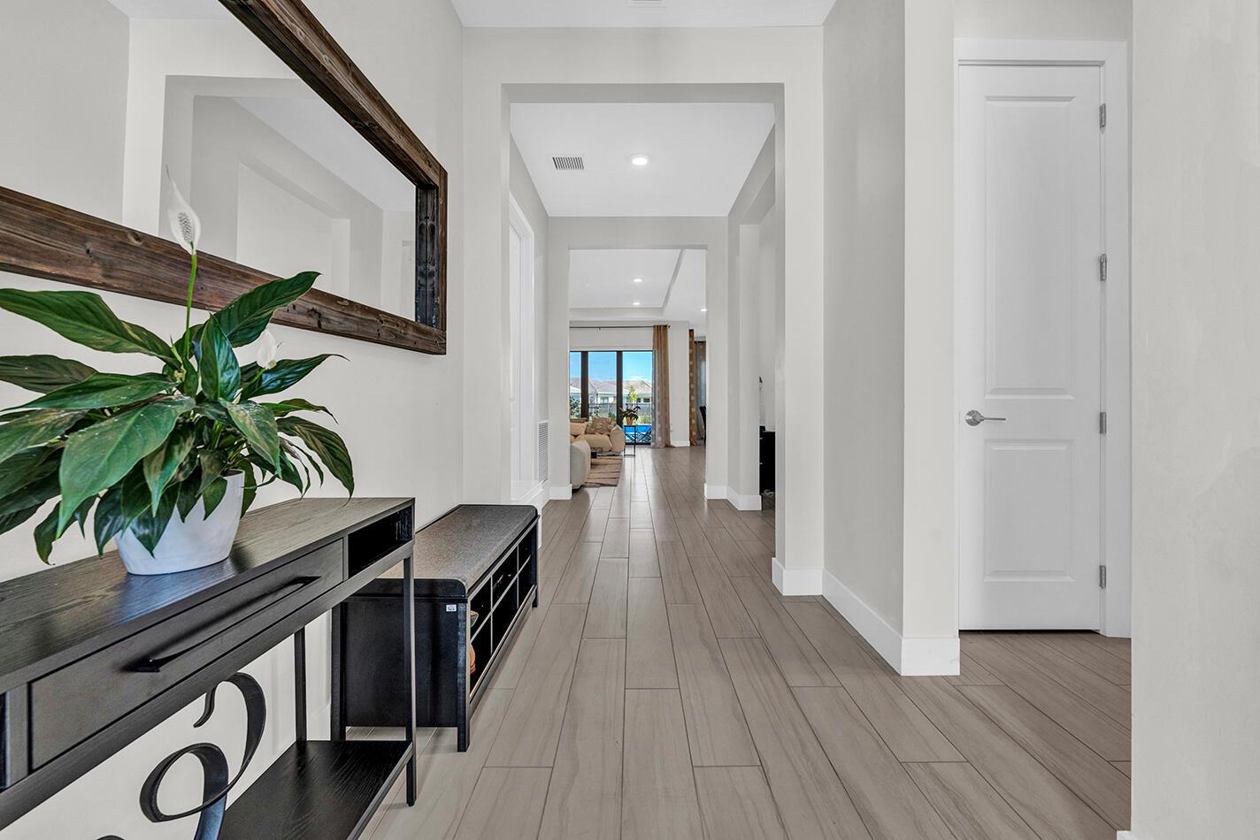 A hallway with wood-look tile flooring leads toward a living area with a view outside — 15647 Merritt Drive, Westlake FL 33470, WESTLAKE, FL