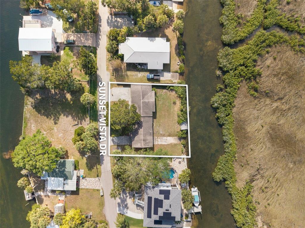 An aerial view shows a house on a lot bordered by a road and canal — 3037 SUNSET VISTA DRIVE, SPRING HILL, FL