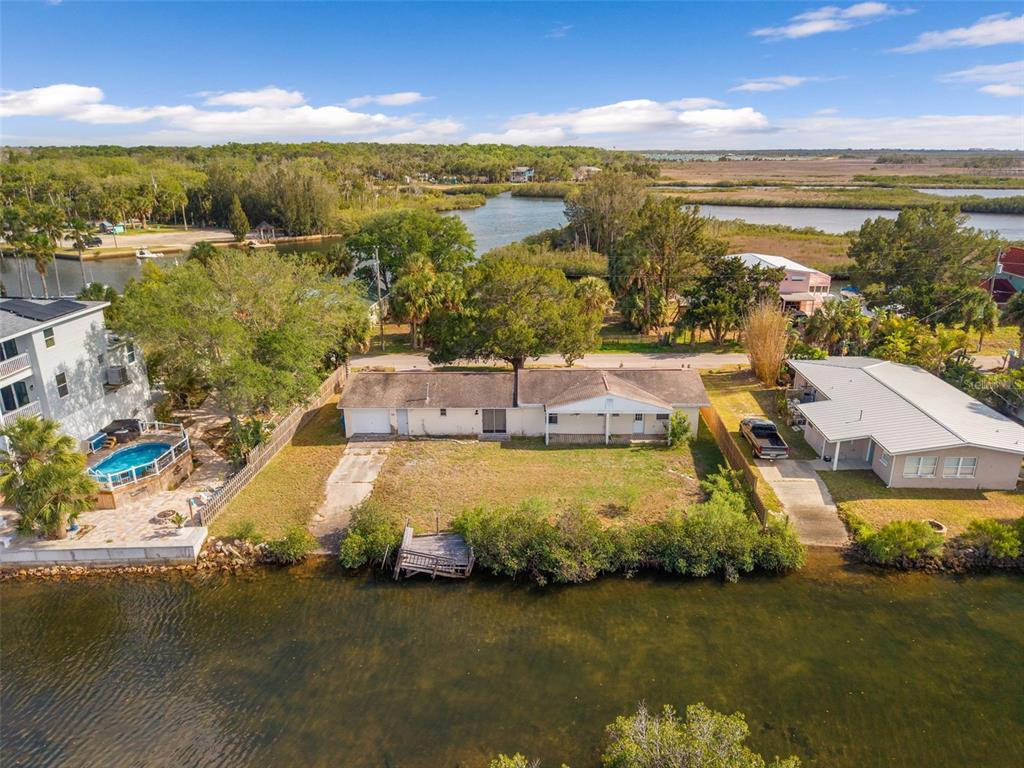 An aerial view shows a waterfront house with a yard, dock, and surrounding vegetation — 3037 SUNSET VISTA DRIVE, SPRING HILL, FL