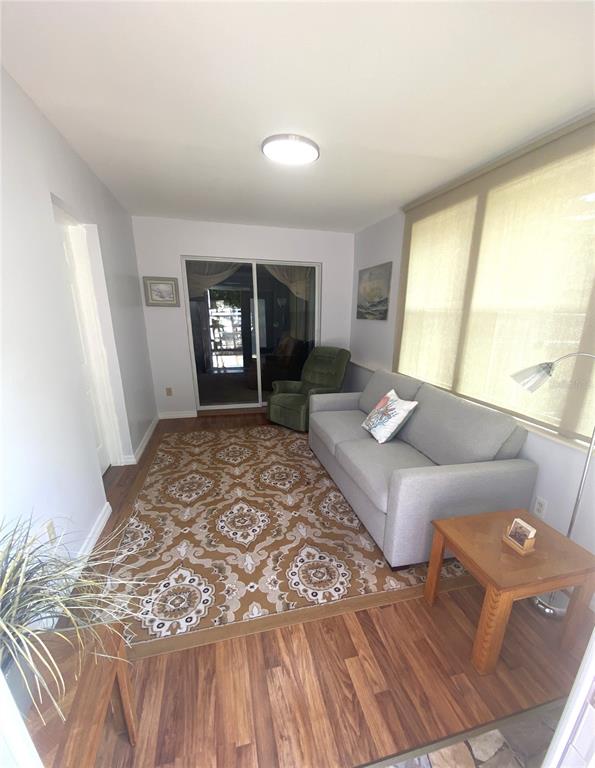 A sunroom features a gray sofa, patterned area rug, wood-look flooring, and a sliding glass door — 829 E 12TH AVENUE, NEW SMYRNA BEACH, FL