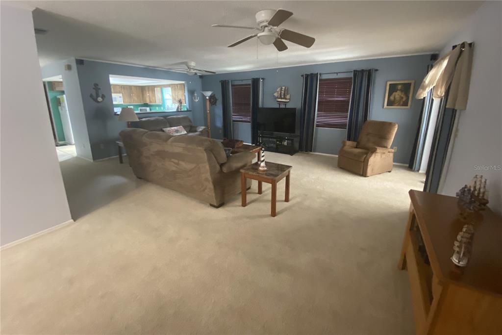 A living room with beige carpet, a brown sofa, a recliner, and a ceiling fan — 829 E 12TH AVENUE, NEW SMYRNA BEACH, FL