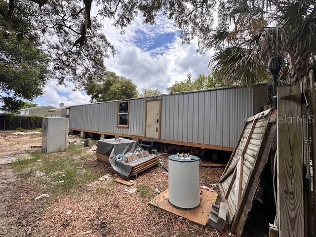 A long, light-colored mobile home sits on a dirt lot under large trees — 6631 CELESTE LANE, NEW PORT RICHEY, FL