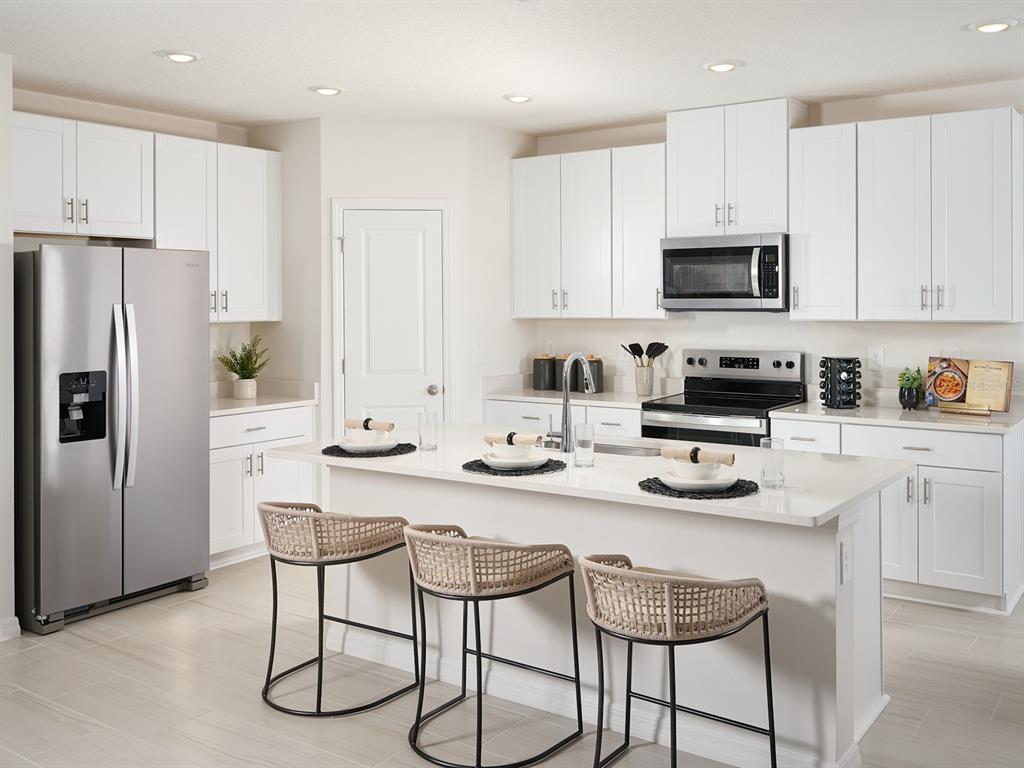 A modern kitchen features white cabinetry, stainless steel appliances, and a central island with seating — 12610 HOURGLASS WAY, DADE CITY, FL