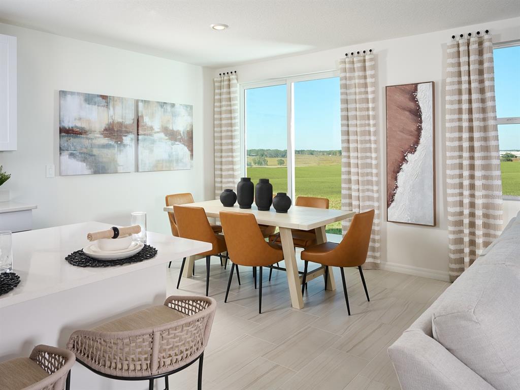 A dining area features a light wood table, tan chairs, and large windows overlooking fields — 12610 HOURGLASS WAY, DADE CITY, FL