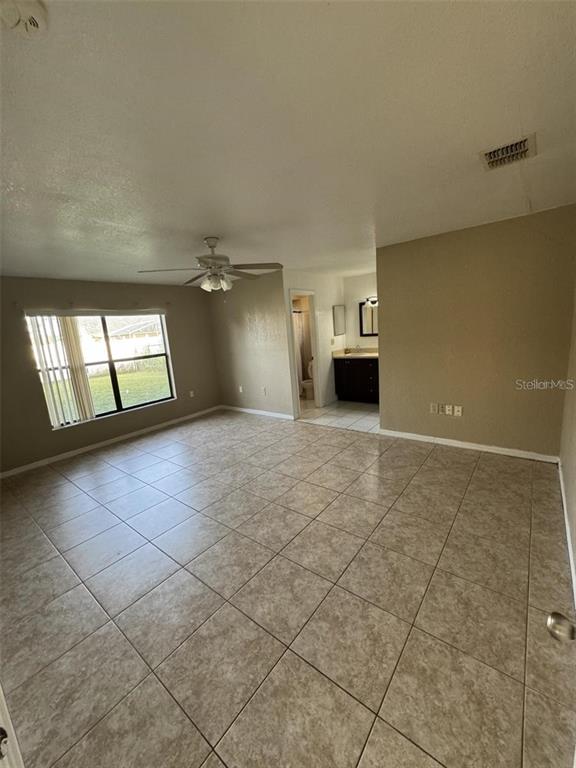 A spacious room with tan tile flooring, a ceiling fan, and an attached bathroom — 913 SAN RAFAEL WAY, KISSIMMEE, FL