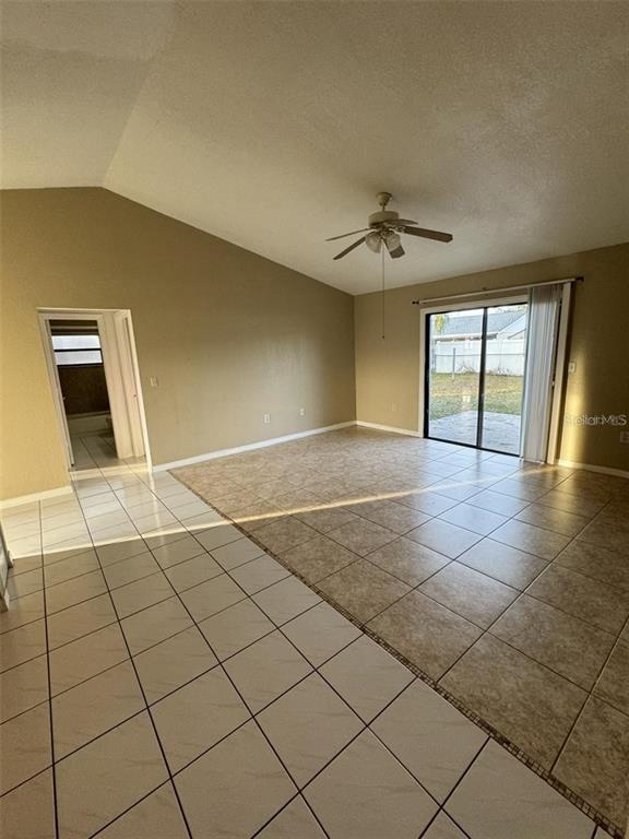 A living room with vaulted ceilings, tile flooring, a ceiling fan, and sliding glass doors — 913 SAN RAFAEL WAY, KISSIMMEE, FL