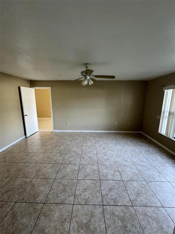 A spacious room with beige tile flooring, tan walls, a ceiling fan, and an open doorway — 913 SAN RAFAEL WAY, KISSIMMEE, FL