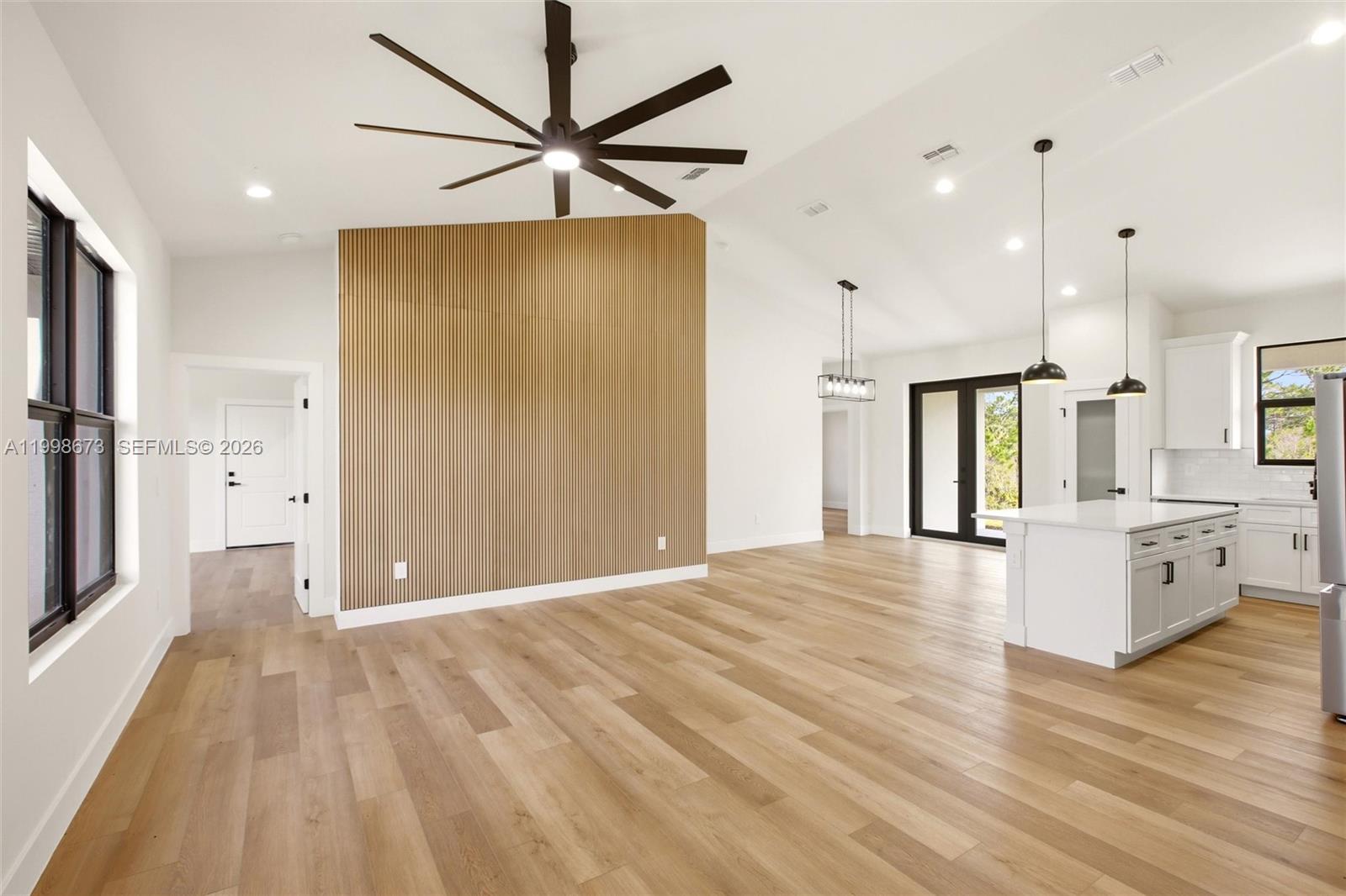 This open-concept living area features light wood flooring, a slatted wood accent wall, and a kitchen — 7322 Granada Boulevard, Sebring FL 33872, SEBRING, FL